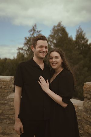 A happy couple wearing matching black outfits poses together on rocky terrain.