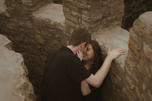A couple embraces passionately between rustic stone walls.