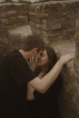 A romantic moment shared between two people against a rustic stone wall backdrop.