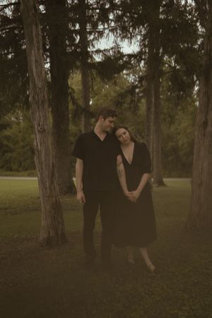 A couple shares an intimate dance beneath towering evergreen trees in a park.