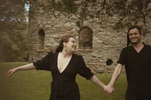 Two people share laughter and smiles in front of an old stone wall.