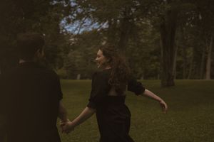 A couple in black clothing share an intimate moment against a natural outdoor backdrop.