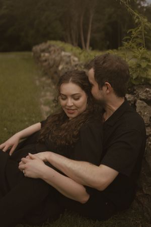 Two people in dark attire share affectionate moments against a natural backdrop.