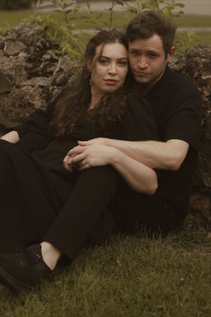 A couple shares tender moments while sitting together near a stone wall outdoors.