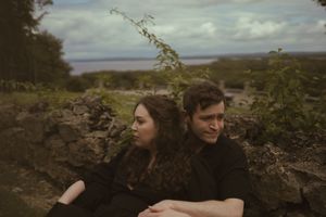 Two people in black clothing share romantic moments in a natural setting.