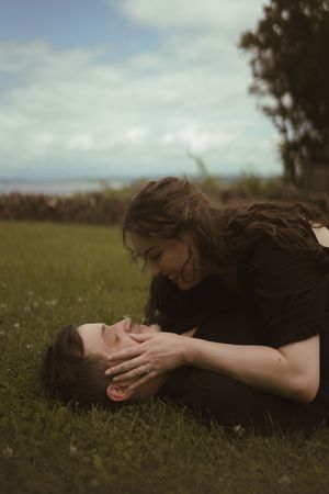 A couple lies in the grass sharing intimate moments under cloudy skies.