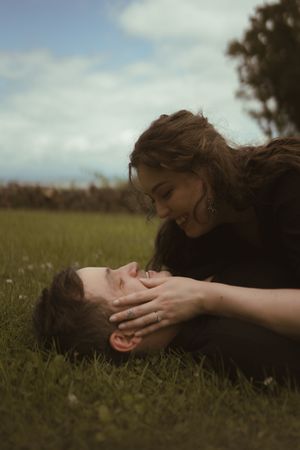 Two people share tender moments while lying in grass under an overcast sky.