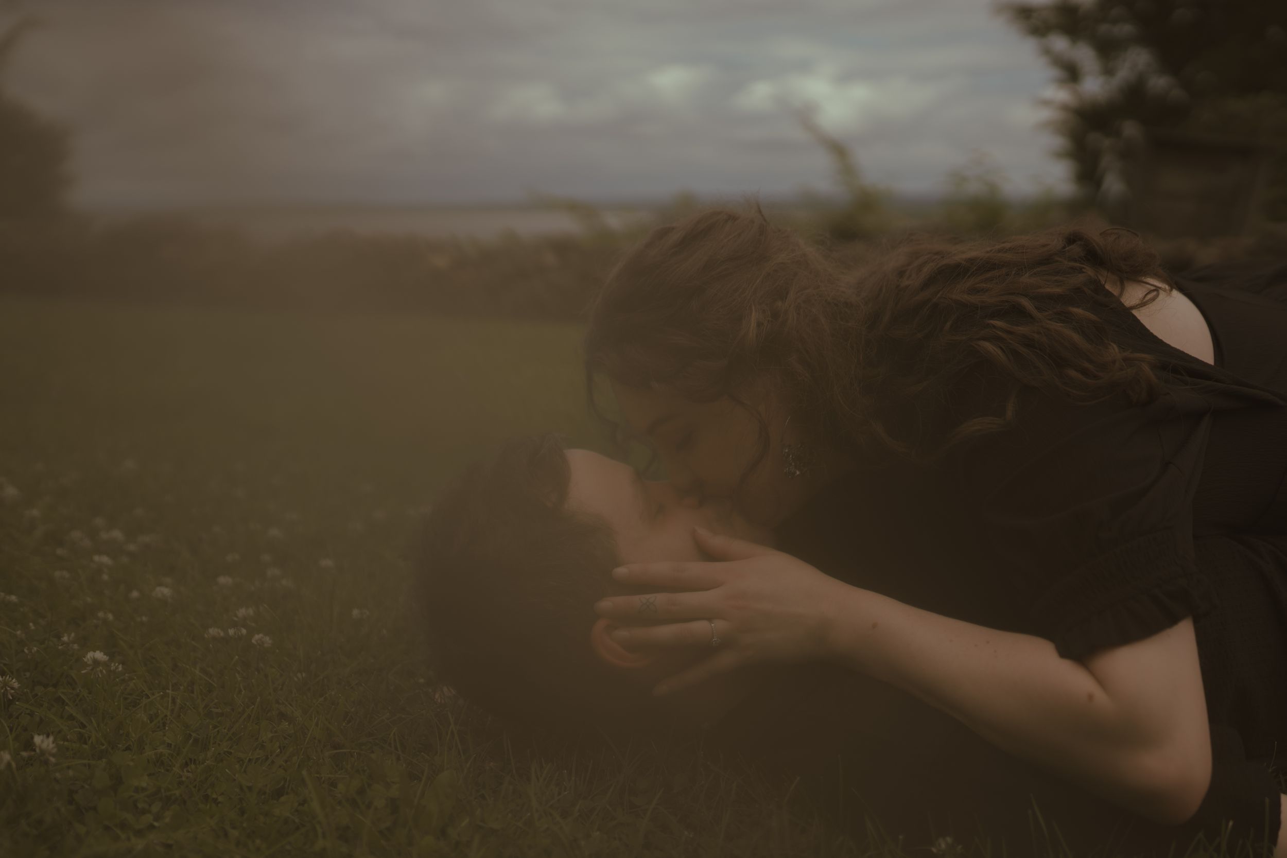 A person leans forward in a moody outdoor setting with wildflowers.