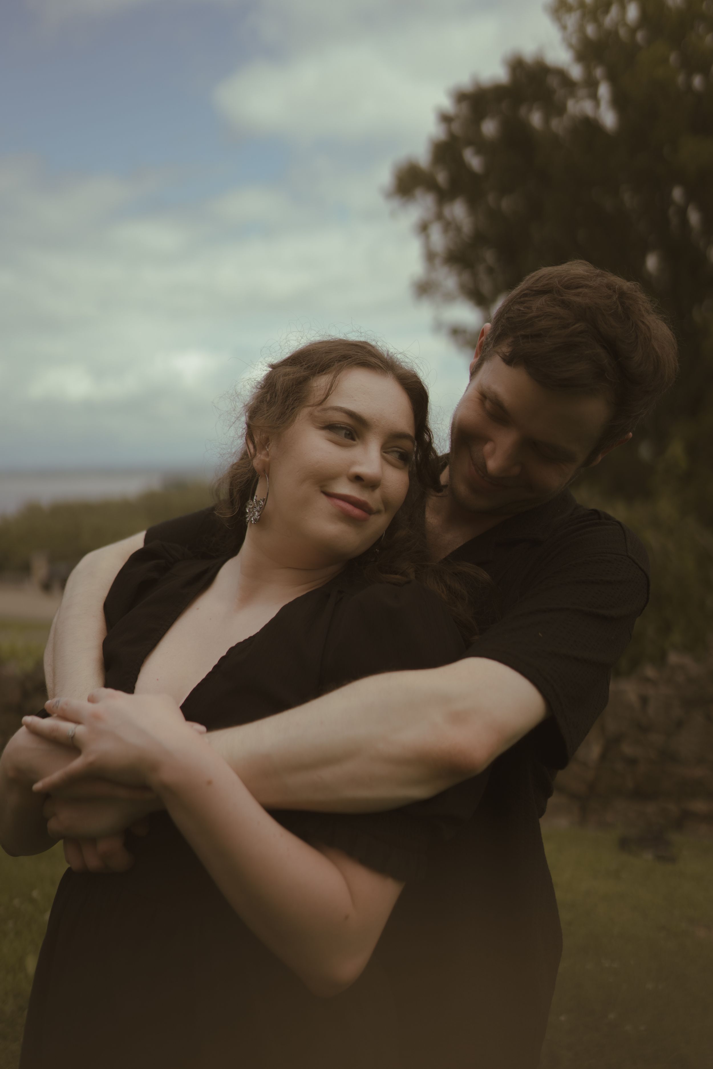 A couple shares an intimate embrace against a cloudy coastal backdrop.