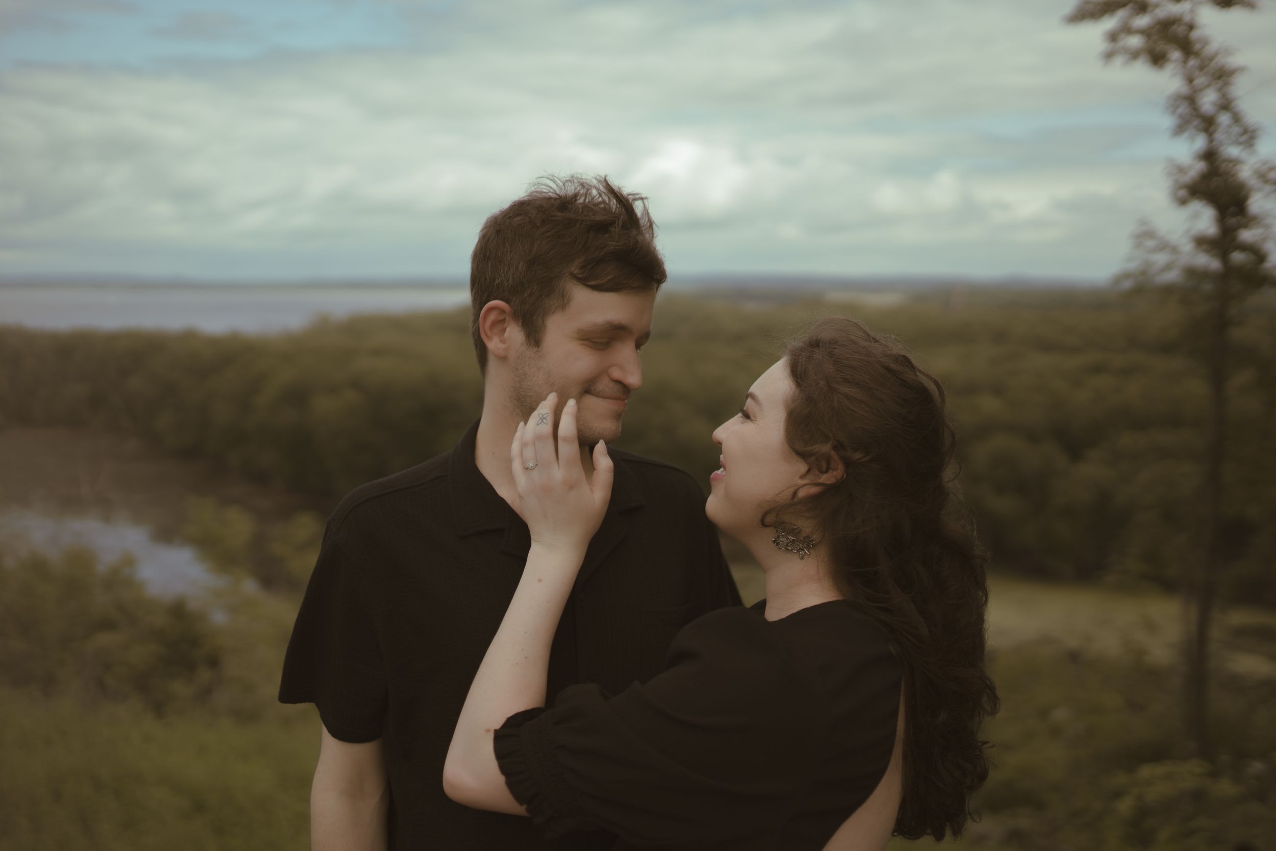 A tender moment between a couple against a scenic landscape backdrop.