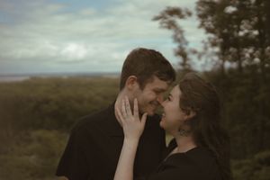 Romantic couple sharing an intimate moment against a cloudy sky backdrop.