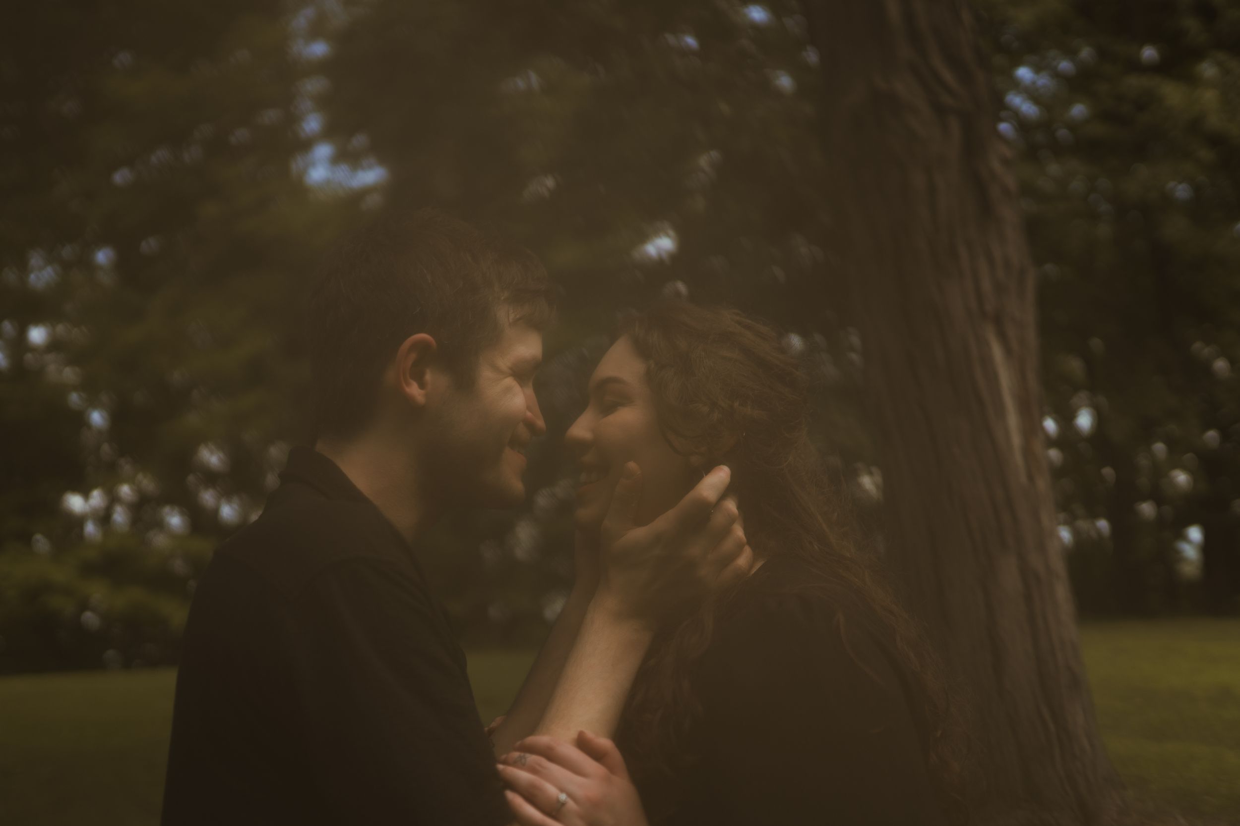 An intimate portrait of a couple in dark clothing against natural foliage.