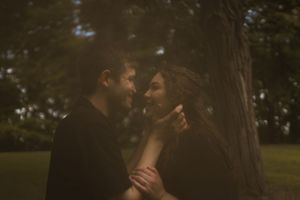 A romantic outdoor photoshoot with two people embracing in dappled sunlight.