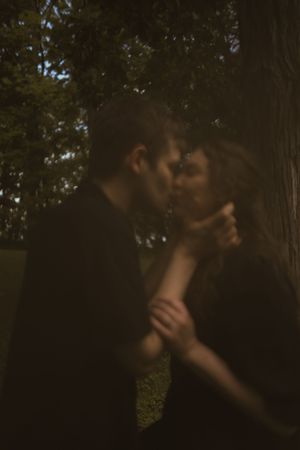 A couple shares a close moment together in a moody forest setting.