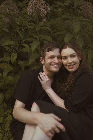 A joyful couple wearing black embraces among flowering bushes in a garden setting.