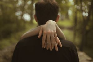 Two figures embracing outdoors with a soft, natural bokeh background.
