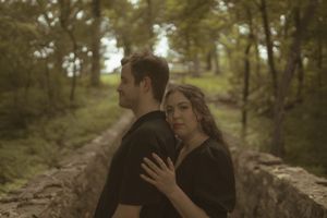 A romantic couple sharing an intimate moment in a wooded setting.