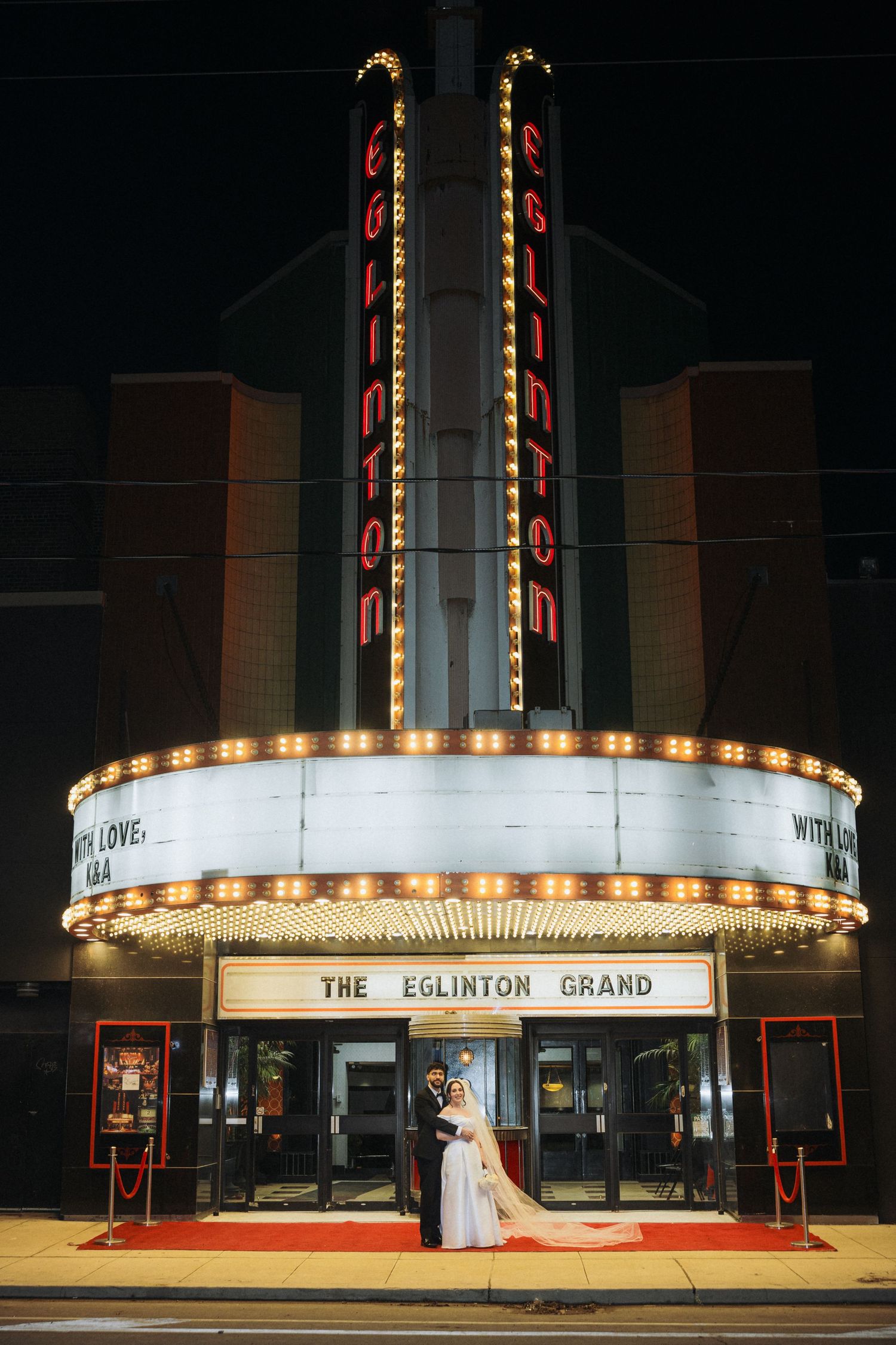 Nighttime exterior view of The Eglinton Grand theatre with illuminated marquee and art deco architectural details.