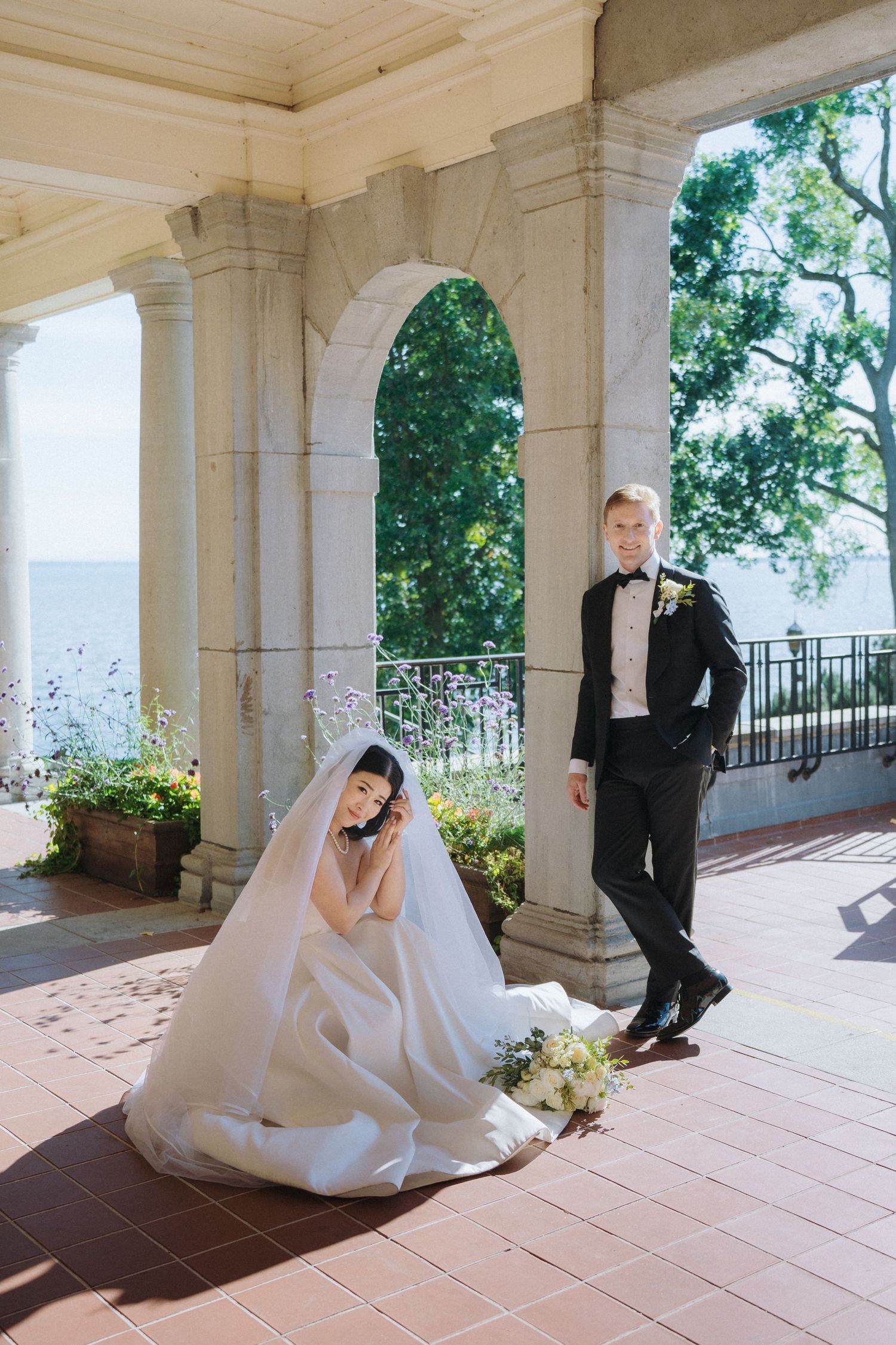 A wedding couple poses playfully in a series of photos along a columned porch with terracotta tiles and garden views.