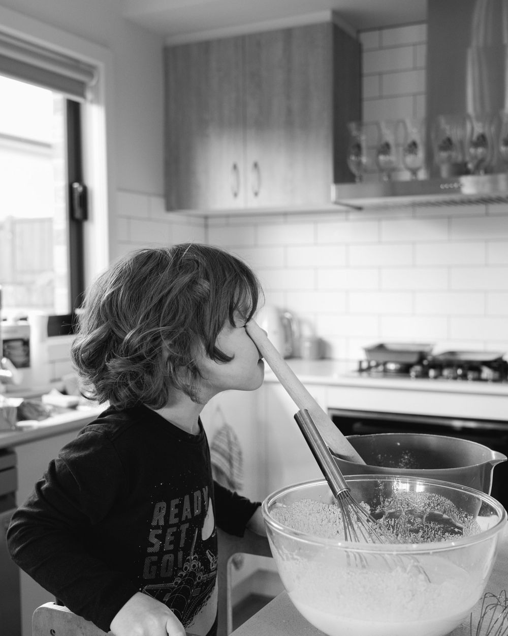 Young child puts  wooden spoon near his eye while cooking in the kitchen with his parent