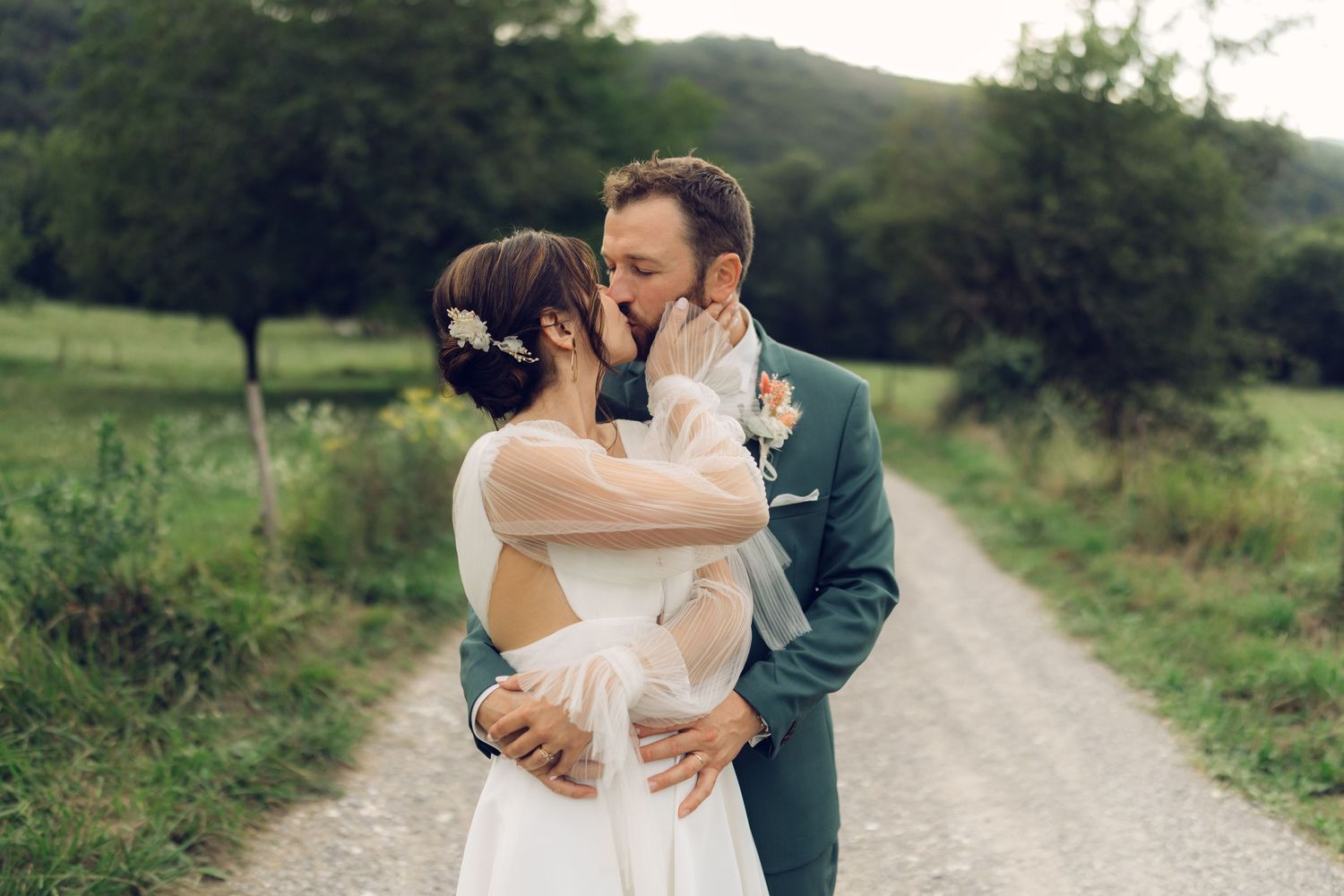 A romantic wedding couple shares their first kiss on a countryside path.