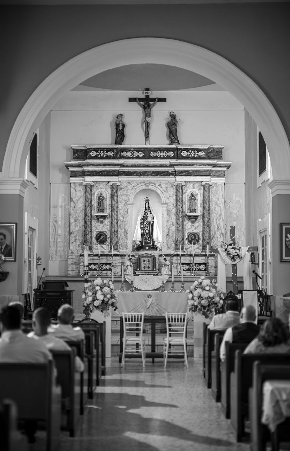 Interior of a traditional Catholic church with ornate altar and floral decorations viewed through an arched entrance.