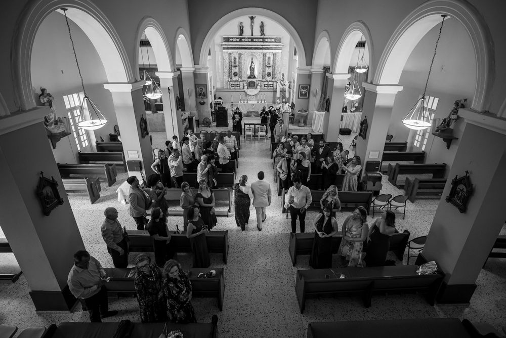 A black and white aerial view of a traditional church ceremony with attendees seated in wooden pews beneath arched architecture.