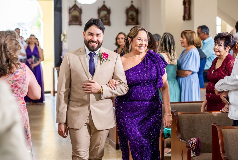A happy pair in formal attire walk down the church aisle as guests smile and celebrate during a joyous ceremony.