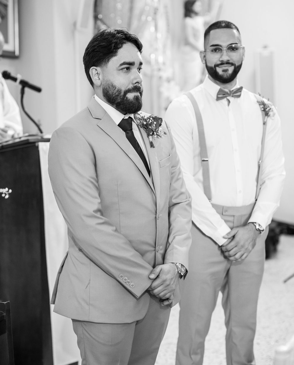 Two wedding participants in formal attire standing at the altar dressed in gray suits and bow ties.