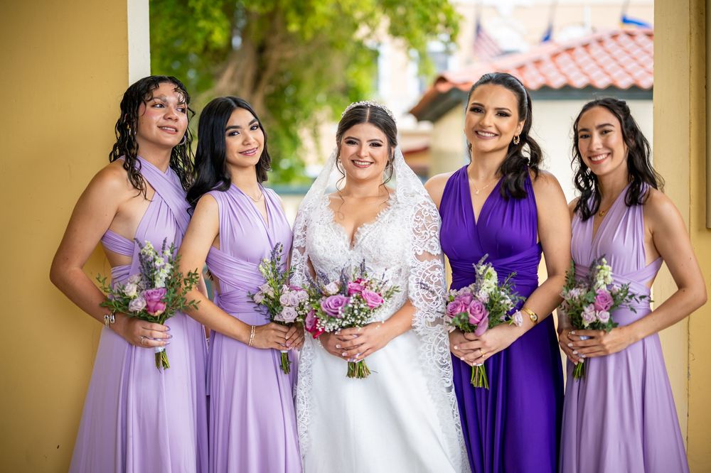 Wedding party wearing coordinated purple and lavender dresses holding vibrant purple and white floral bouquets.