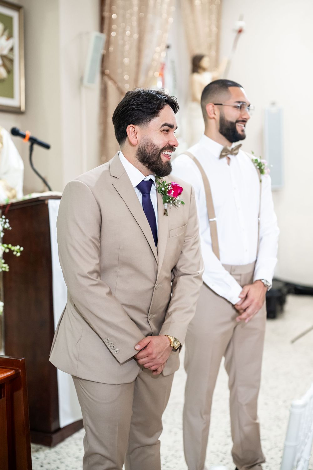 Two wedding attendants share a joyful moment while wearing coordinating beige and white suits.