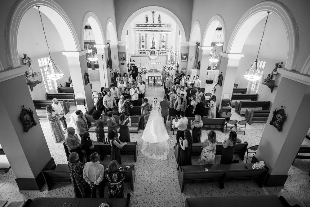 Overhead view of a traditional Catholic church wedding ceremony with guests seated in pews beneath arched architecture.