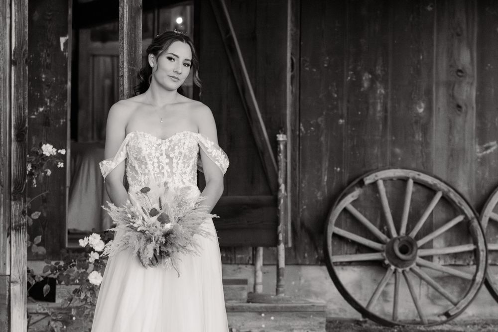 Bride in a white lace wedding dress poses in a rustic barn setting with string lights and wooden decor.