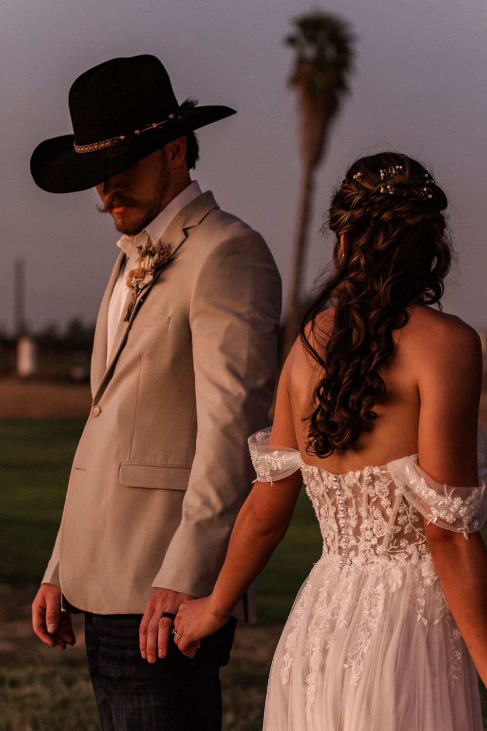 Sunset wedding portrait of couple in western attire against dusky sky.
