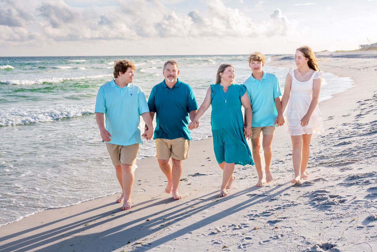 Group of people standing together on a white sandy beach with turquoise waves and cloudy sky in the background.