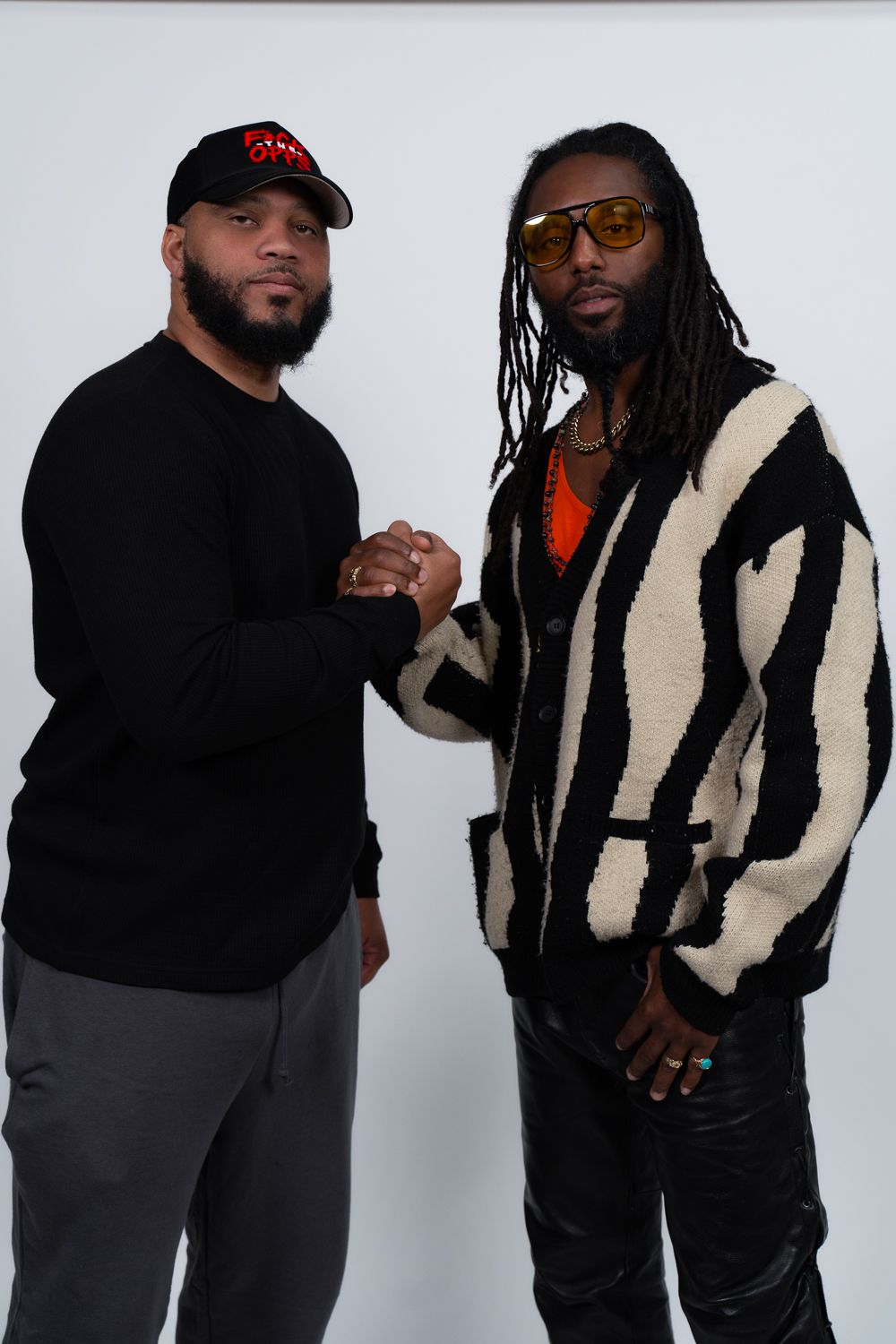 Hip hop artists pose together in black outfits against white background for artistic photo series.