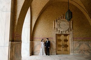 A couple stands beneath an arched passageway with decorative stonework and vintage architectural details.