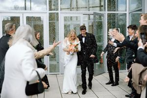 Guests throw confetti as newlyweds exit their wedding ceremony through modern glass doors.