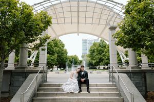 Panoramic view of wedding couple in a covered outdoor walkway with white arched roof and green trees.