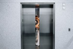 Person peeking through partially open elevator doors in a modern building.