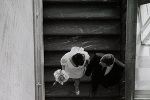 Black and white overhead view of a couple descending wooden stairs with a wedding bouquet.