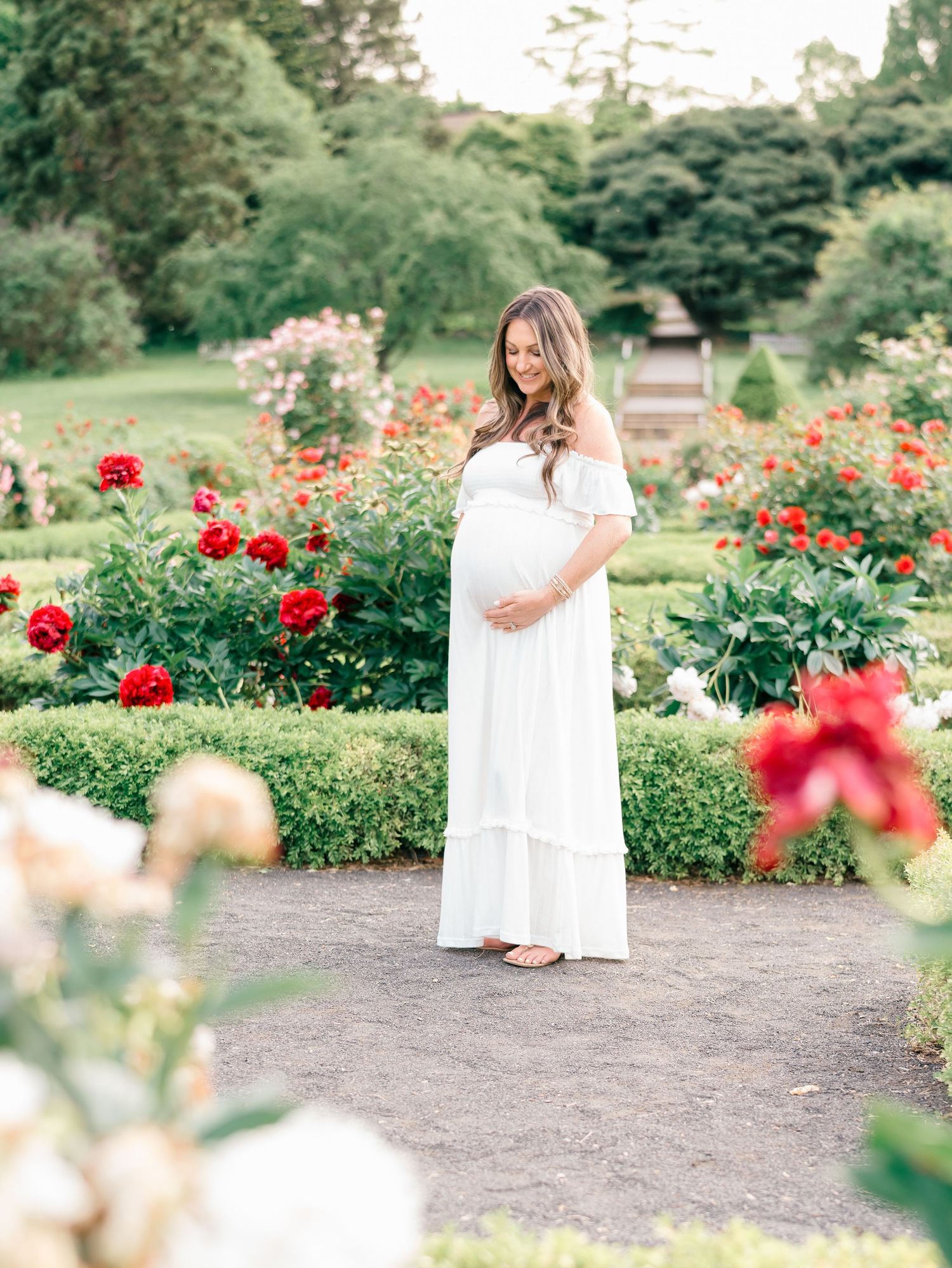 Expecting mother standing among colorful flowers, gently holding her belly during a maternity shoot.