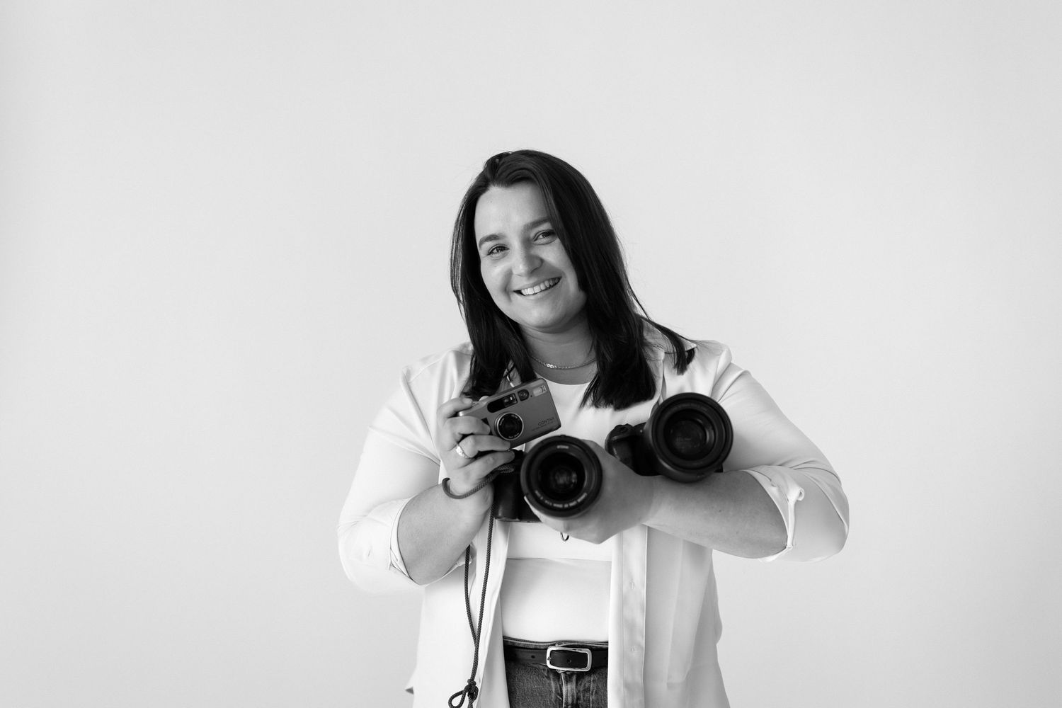 A photographer smiles while holding professional camera equipment against a white background. Both digital and film