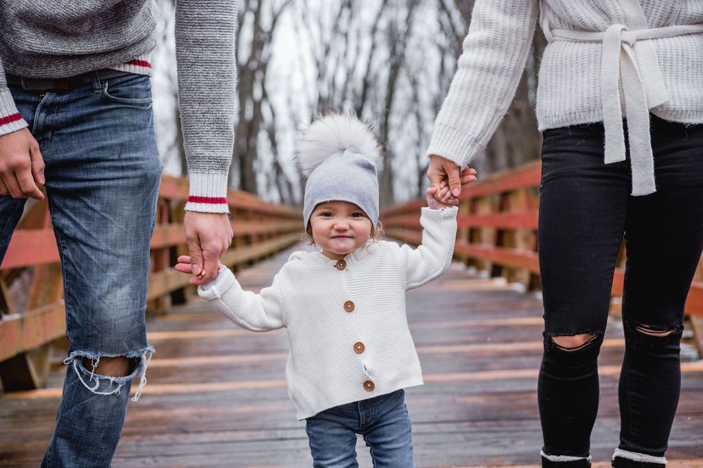 A child in a white cardigan walks with adults on a wooden bridge during winter.