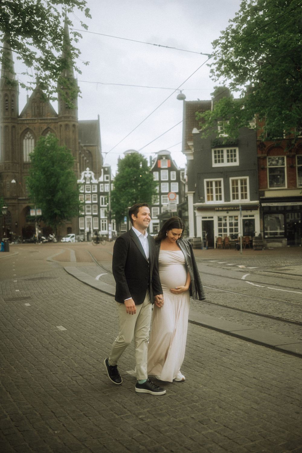 Couple walking through a historic Amsterdam square with traditional Dutch buildings.