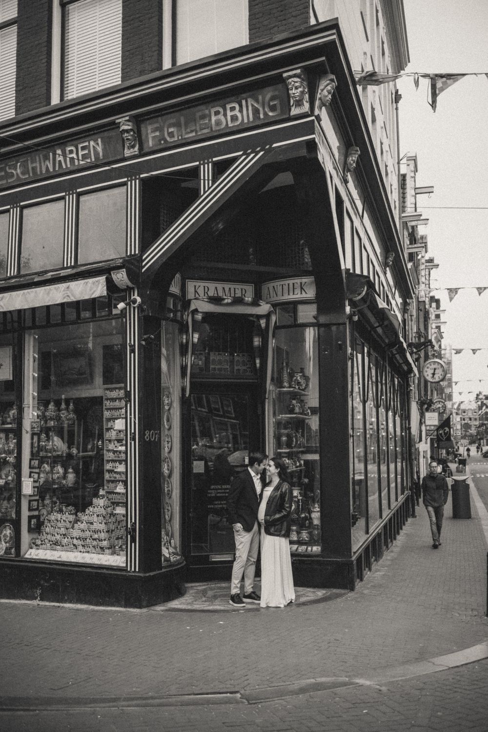 Black and white photo of vintage storefronts in Amsterdam with Dutch signage.