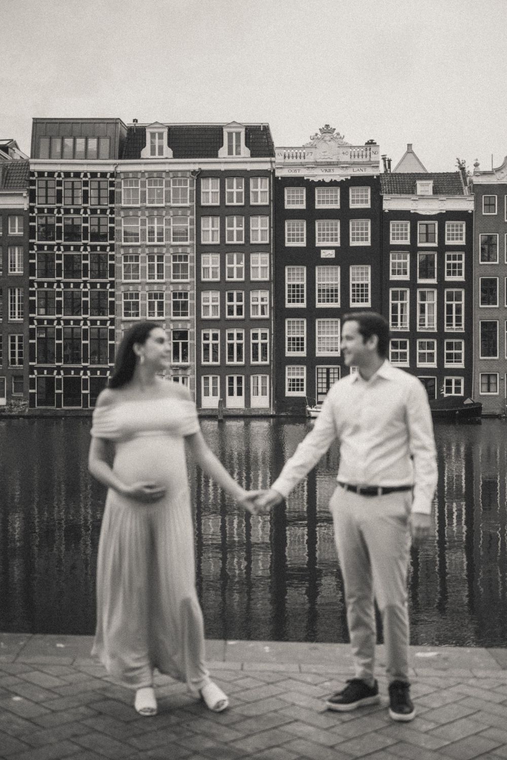 A black and white series showing playful moments between a couple by Amsterdam's waterfront buildings.