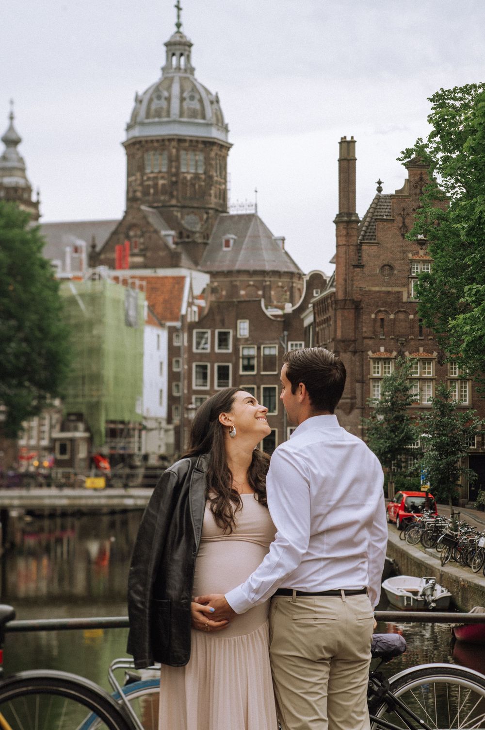 A couple shares romantic moments along Amsterdam's historic canals with classic Dutch architecture in the background.