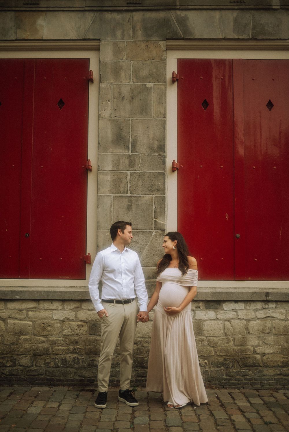 Couple posing against red doors and stone walls in a historic European setting.