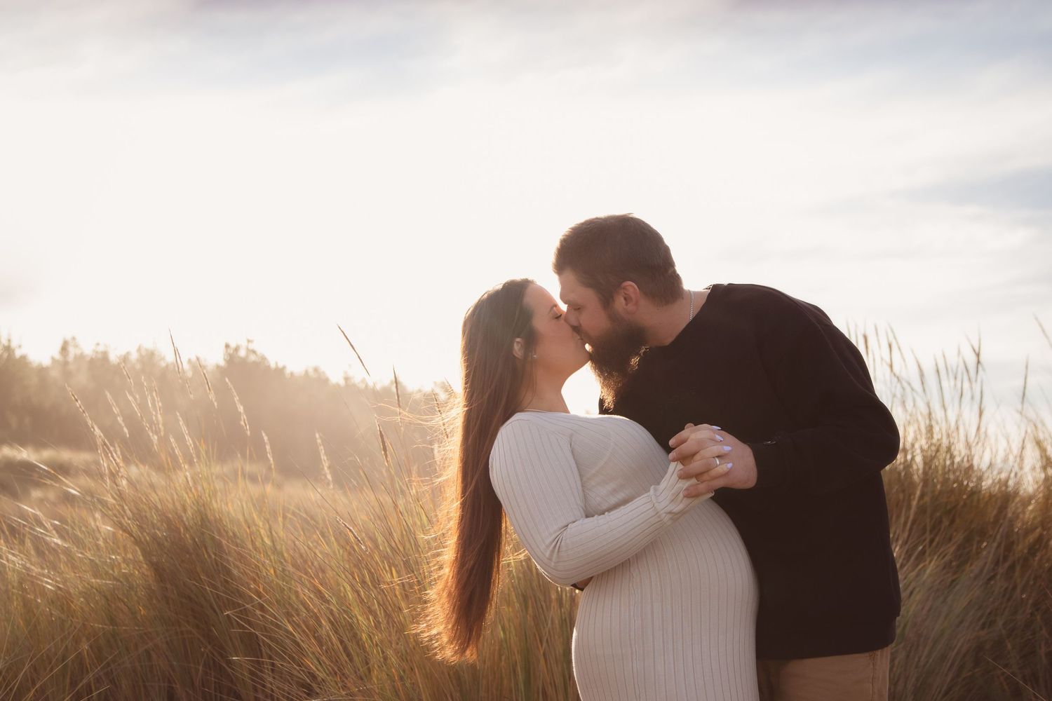 Romantic couple embracing in golden sunlit field during sunset engagement photo session.